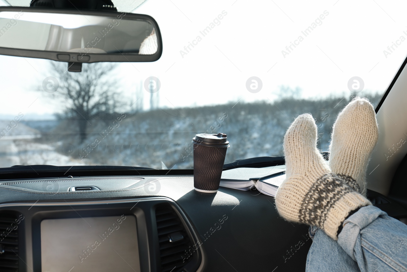 Photo of Young woman in warm socks holding her legs on car dashboard. Cozy atmosphere