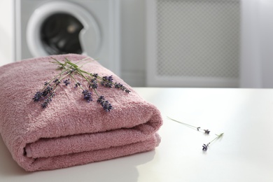 Photo of Folded clean towel and lavender flowers on white table indoors. Space for text