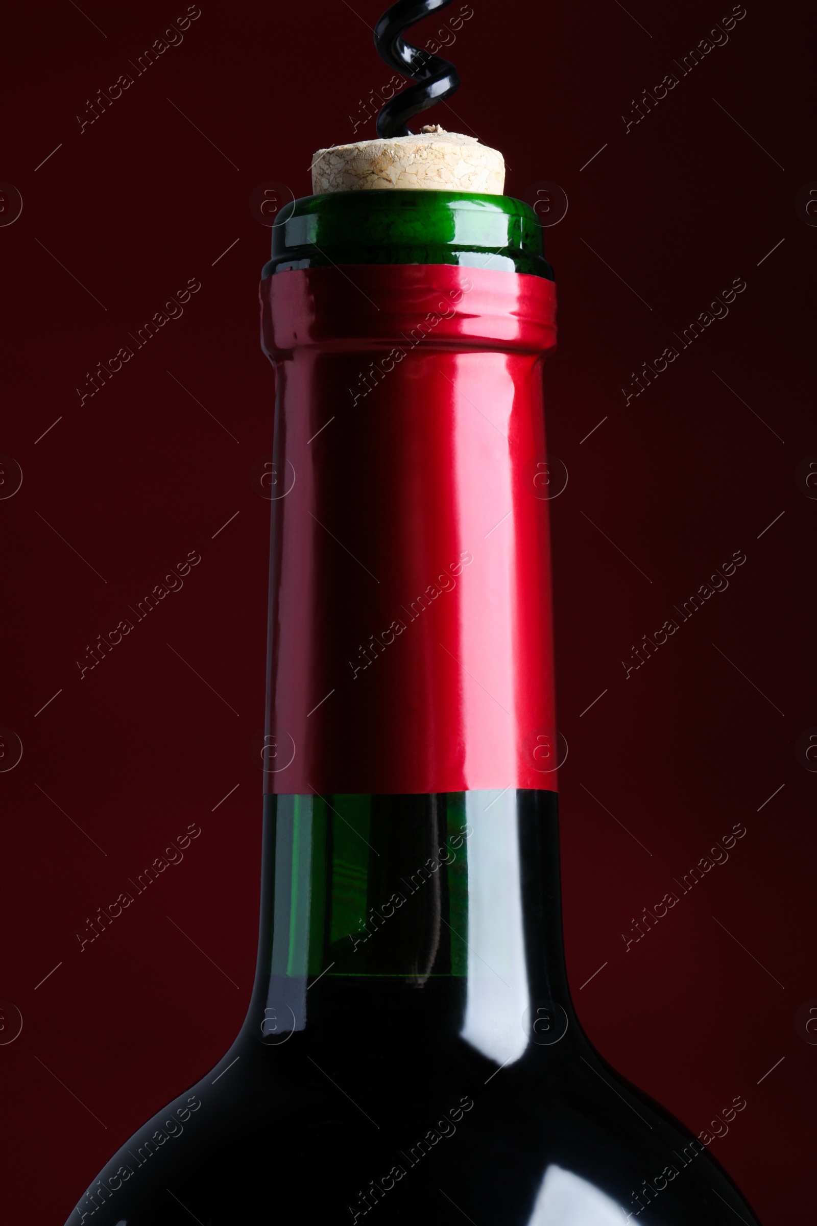 Photo of Opening bottle of wine with corkscrew on burgundy background