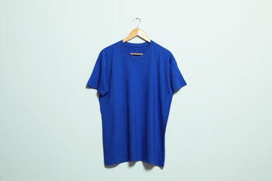 Photo of Hanger with blue t-shirt on light wall. Mockup for design