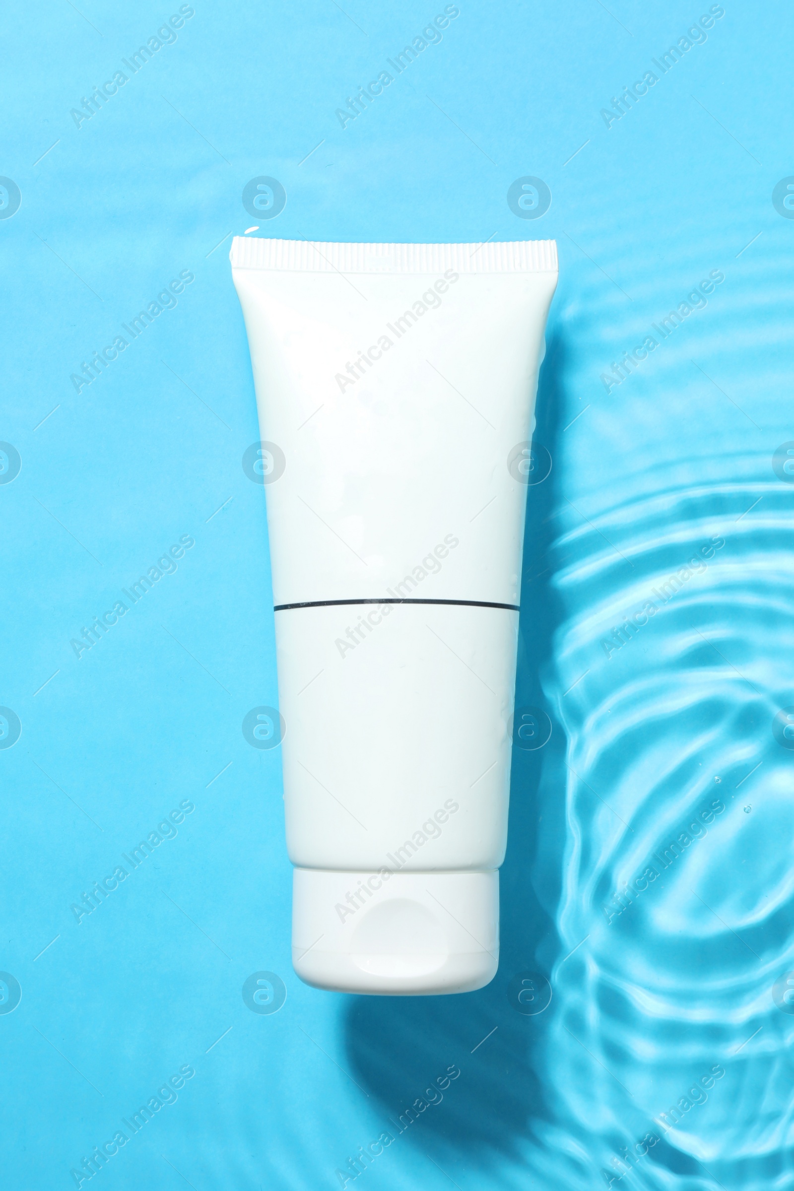 Photo of Tube with moisturizing cream in water on light blue background, top view