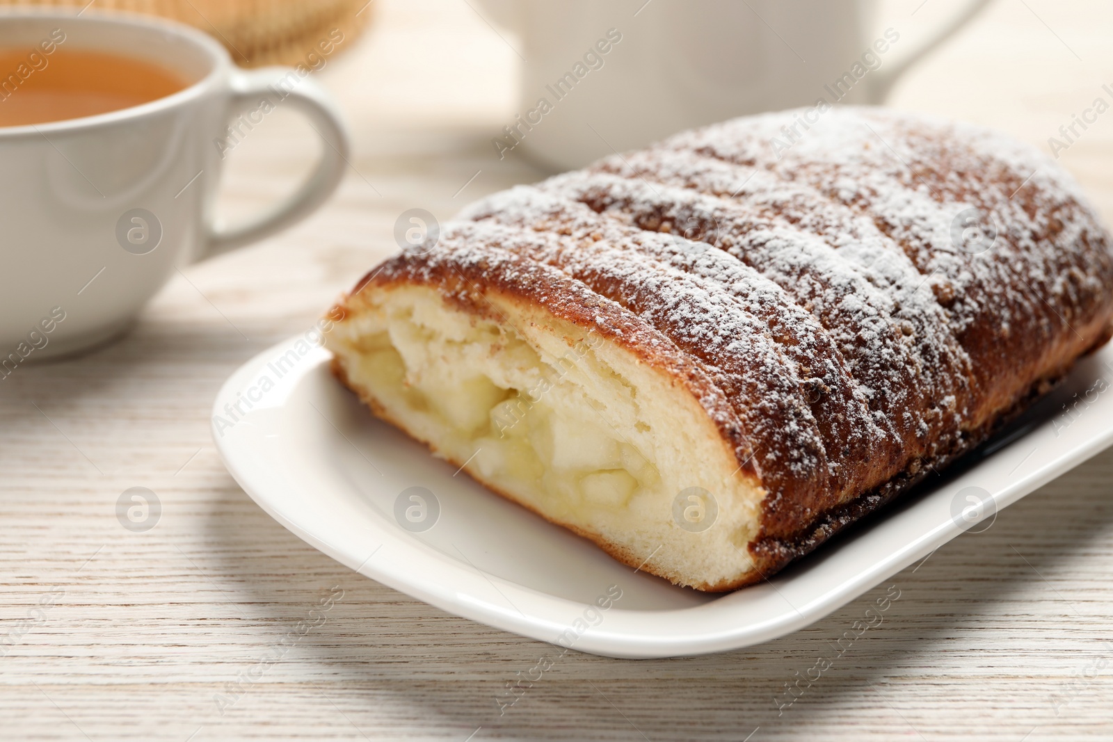 Photo of Delicious yeast dough cake and tea on wooden table, closeup