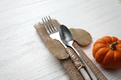 Photo of Cutlery with leaves and pumpkin on white wooden background, closeup. Table setting elements