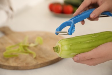 Photo of Woman peeling zucchini in kitchen, closeup with space for text. Preparing vegetable