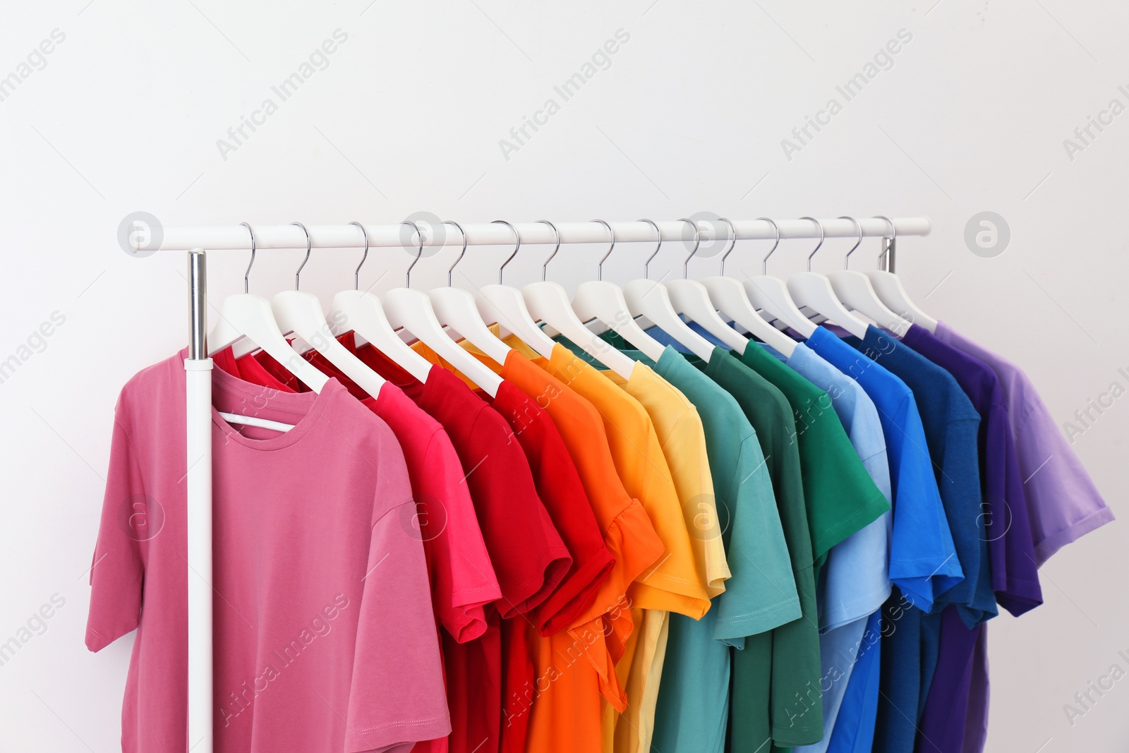 Photo of Rack with bright clothes on white background. Rainbow colors