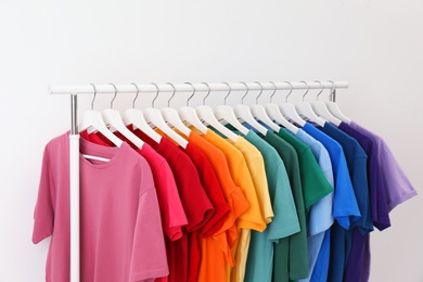 Photo of Rack with bright clothes on white background. Rainbow colors