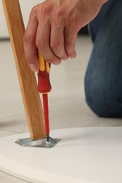 Photo of Man with screwdriver assembling table on floor indoors, closeup