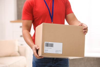 Young courier holding parcel indoors, closeup. Delivery service