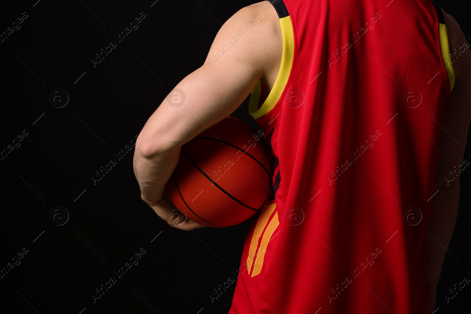 Photo of Athletic man with basketball ball on black background, closeup