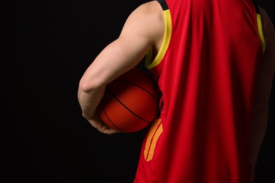 Athletic man with basketball ball on black background, closeup