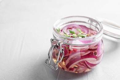 Photo of Jar of pickled onions on grey table. Space for text