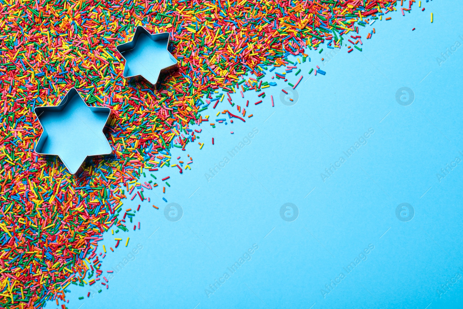 Photo of Star shaped cutters and sprinkles on light blue background, flat lay with space for text. Confectionery decor