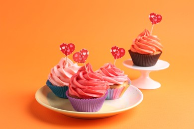 Photo of Delicious cupcakes with bright cream and heart toppers on orange background