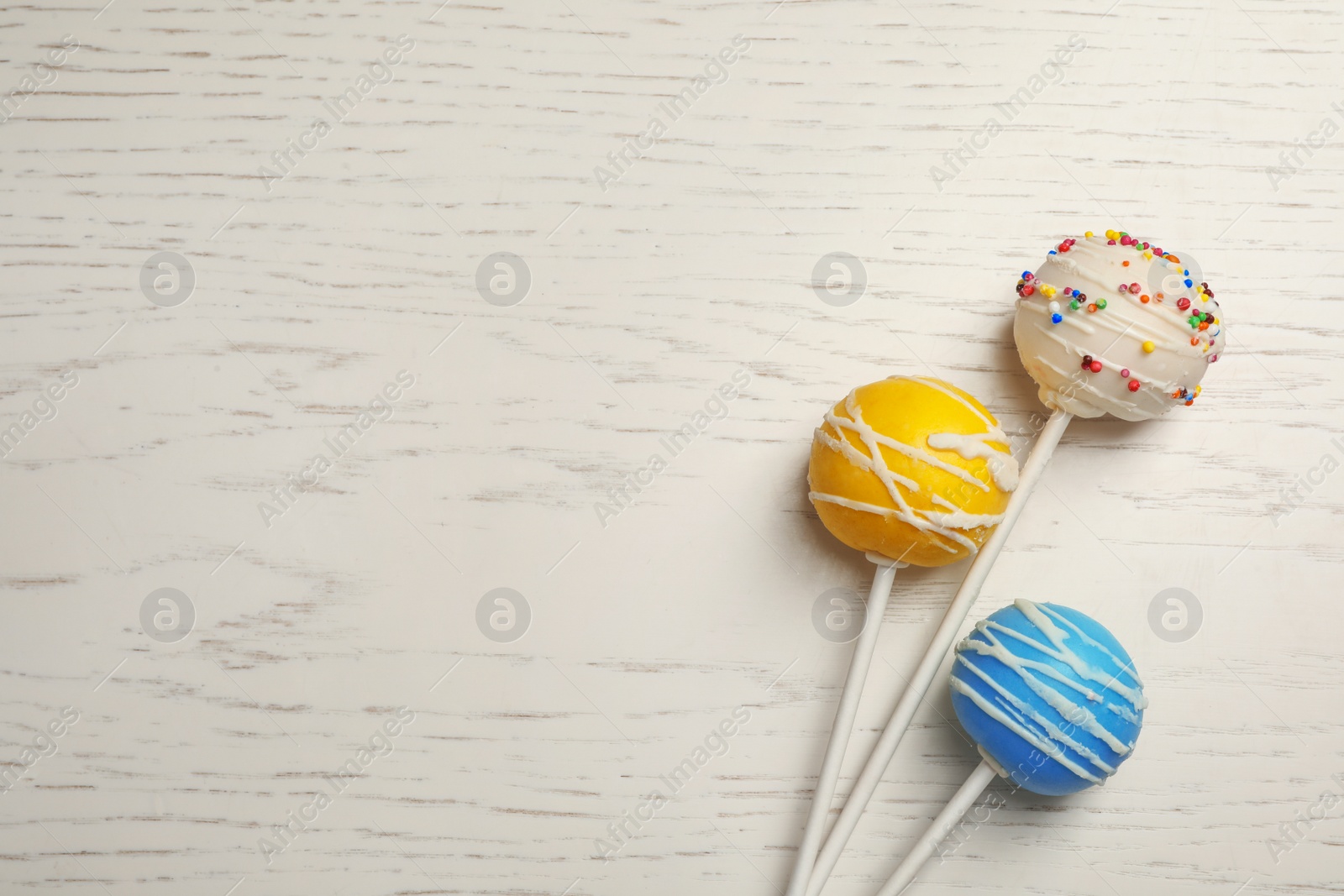 Photo of Bright delicious cake pops on wooden table, flat lay. Space for text