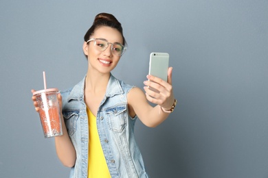 Young beautiful woman taking selfie against grey background