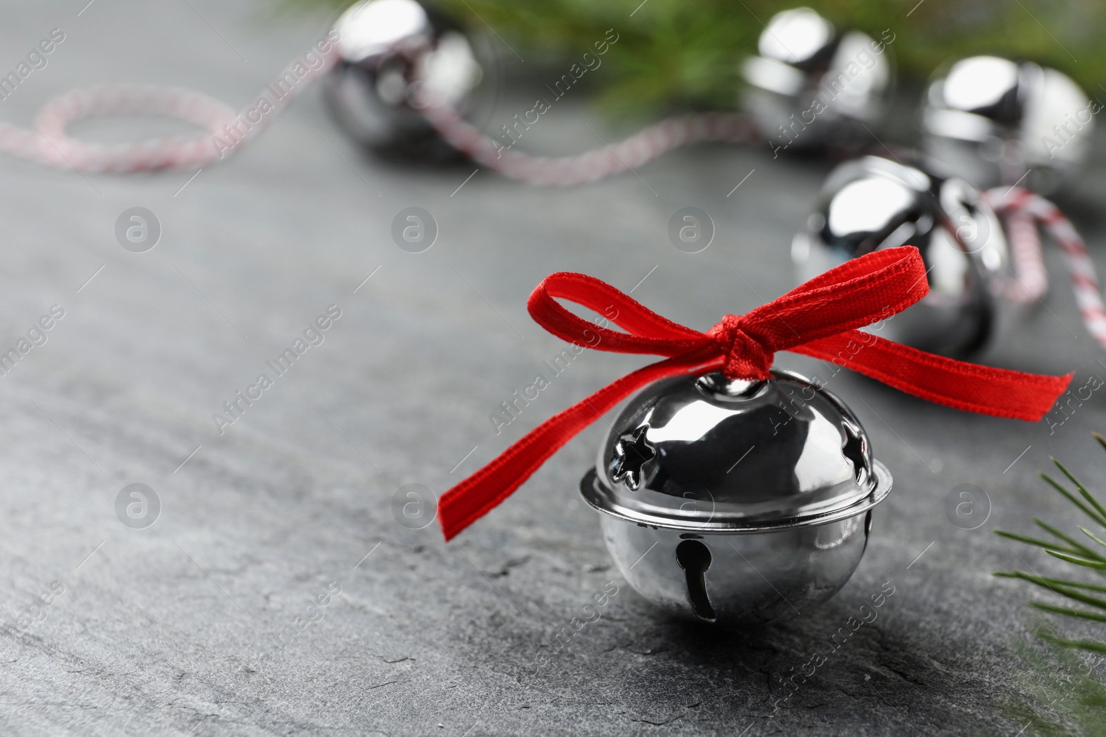 Photo of Shiny silver sleigh bell on grey stone table, closeup. Space for text