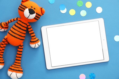 Photo of Modern tablet, confetti and toy tiger on blue background, flat lay. Space for text