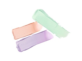 Photo of Strokes of pink, green and purple color correcting concealers isolated on white, top view