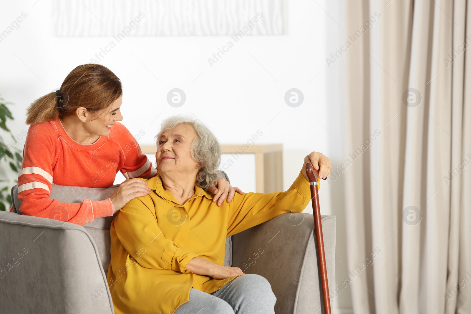 Photo of Elderly woman with female caregiver in living room. Space for text