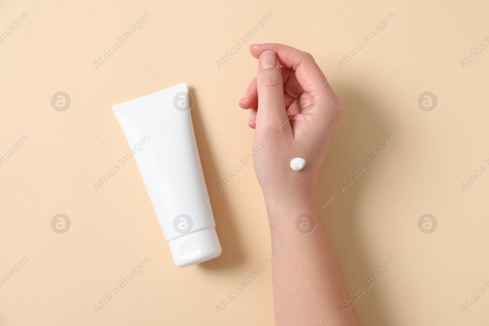 Photo of Woman with tube of hand cream on beige background, top view