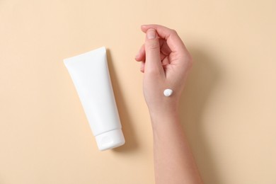 Woman with tube of hand cream on beige background, top view