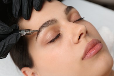 Beautician making permanent eyebrow makeup to young woman, closeup