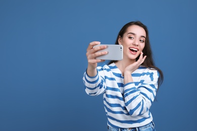 Photo of Attractive young woman taking selfie with phone on color background