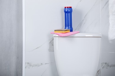 Photo of Bottle, sponge and cleaning rag on toilet bowl in bathroom, space for text