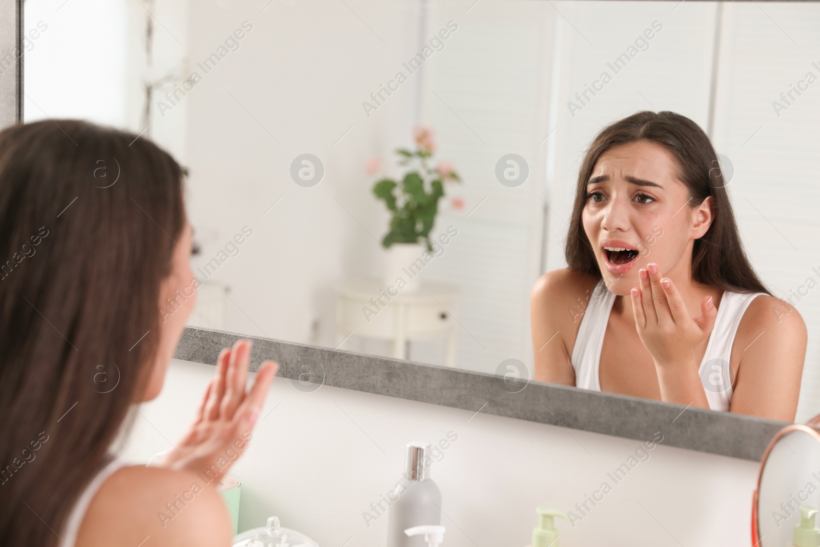 Photo of Young woman with eyelash loss problem looking in mirror indoors