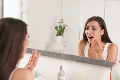 Young woman with eyelash loss problem looking in mirror indoors