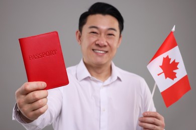 Photo of Immigration. Happy man with passport and flag of Canada on grey background, selective focus