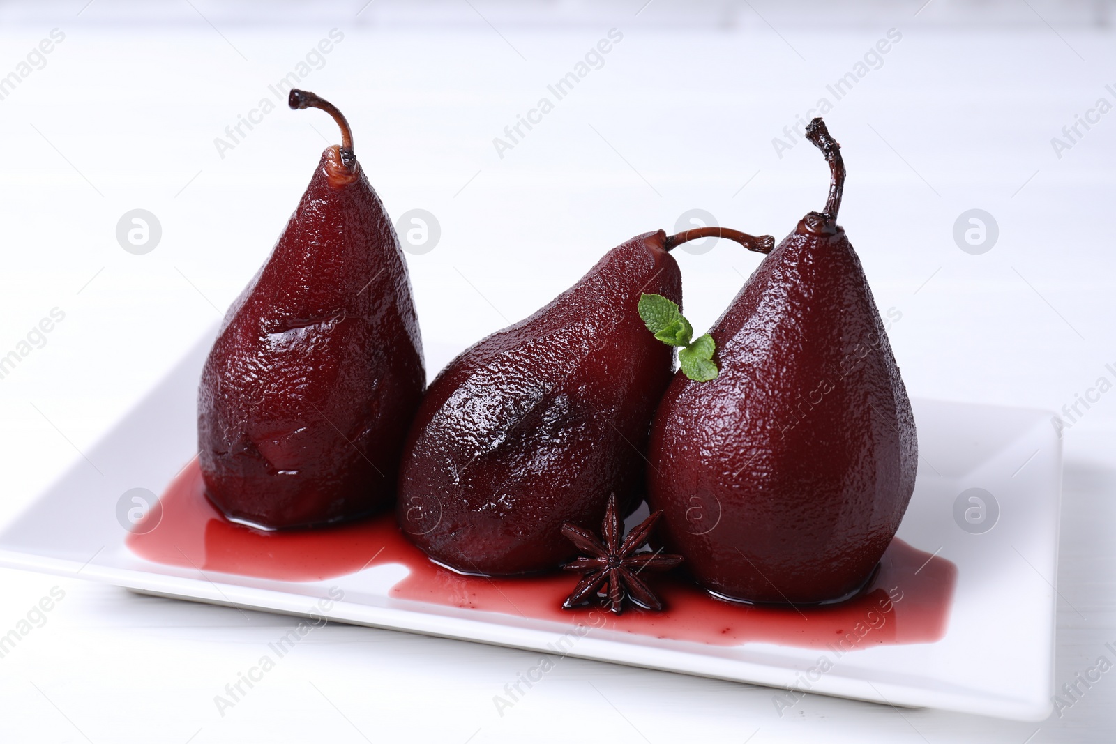 Photo of Tasty red wine poached pears with mint and anise on white wooden table, closeup