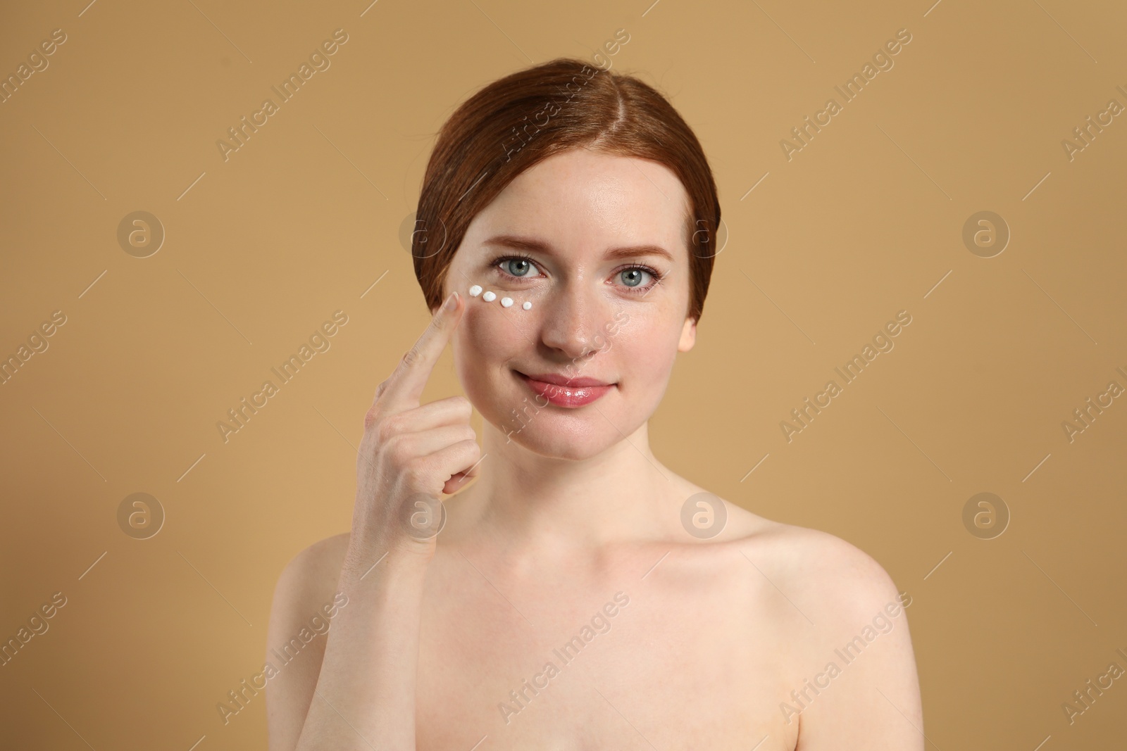 Photo of Beautiful woman with freckles and cream on her face against beige background