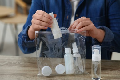 Photo of Woman packing cosmetic travel kit at wooden table indoors, closeup. Bath accessories