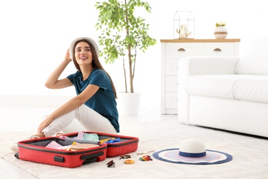 Young woman packing suitcase for summer journey at home