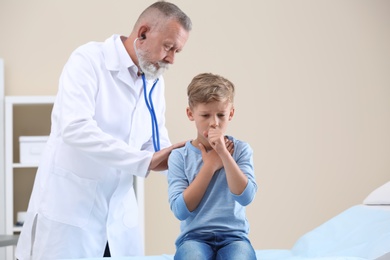 Doctor examining coughing little boy at clinic