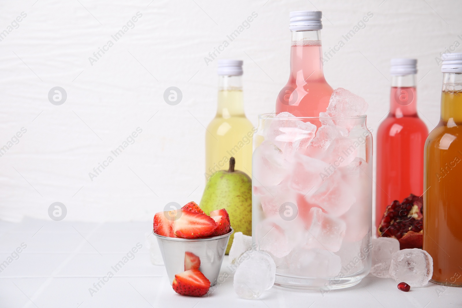 Photo of Tasty kombucha in bottles, glass with ice and fresh fruits on white table, space for text