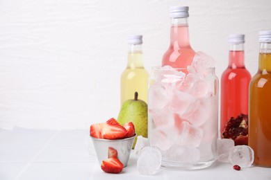 Tasty kombucha in bottles, glass with ice and fresh fruits on white table, space for text