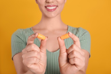 Young woman with foam ear plugs on yellow background, closeup