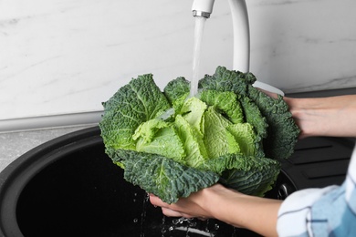 Photo of Woman washing fresh green savoy cabbage under tap water in kitchen sink, closeup