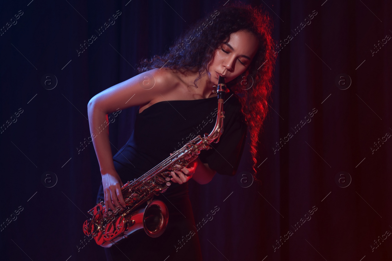 Photo of Beautiful African American woman playing saxophone on dark background