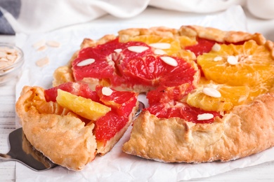 Photo of Tasty galette with citrus fruits and almond flakes on table, closeup