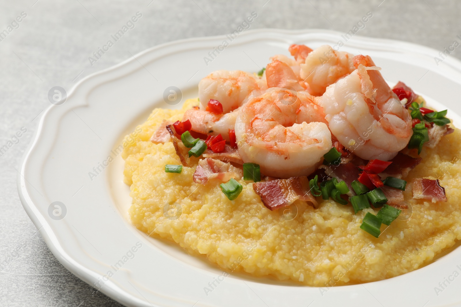 Photo of Plate with fresh tasty shrimps, bacon, grits, green onion and pepper on gray table, closeup