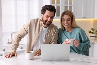 Happy couple with laptop at white table in kitchen