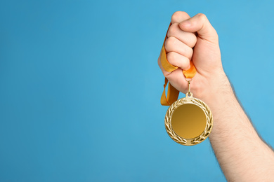 Photo of Man holding silver medal on blue background, closeup. Space for design