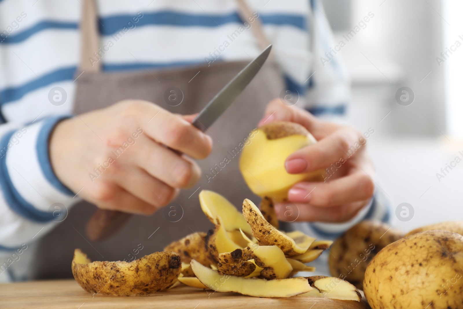 Photo of Woman peeling fresh potato with knife at table, focus on peels