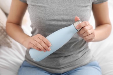 Photo of Woman holding thermo bottle on bed, closeup