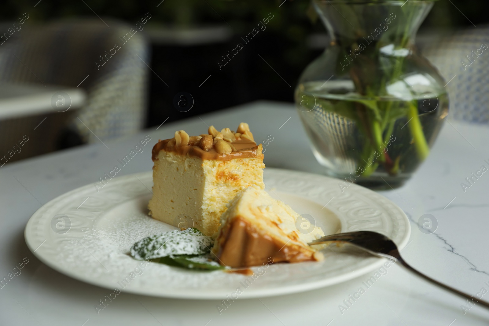 Photo of Tasty dessert and vase with flowers on white table in cafeteria