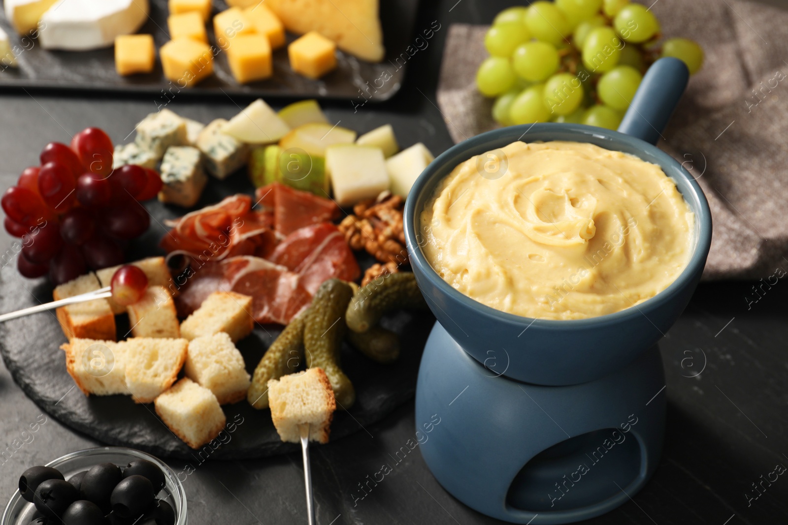 Photo of Fondue with tasty melted cheese, forks and different snacks on black table