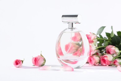 Bottle of luxury perfume and beautiful roses on white background, space for text. Floral fragrance